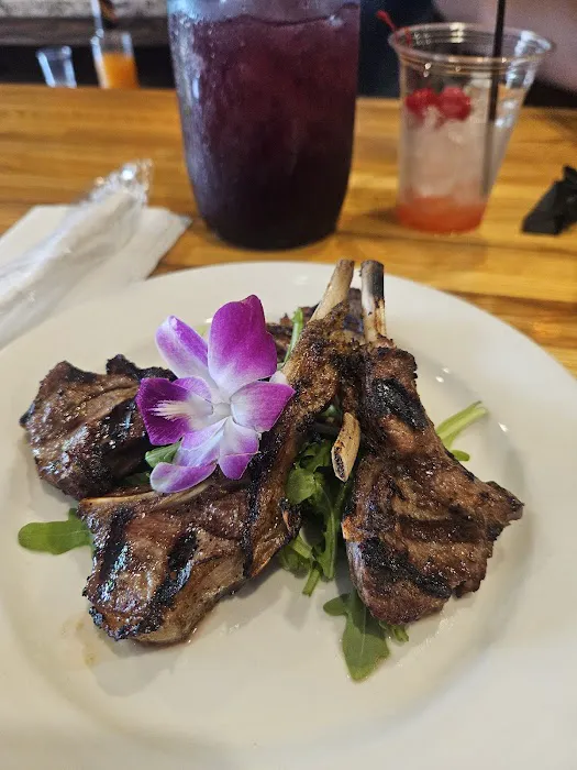 Grilled lamb chops on arugula with an orchid garnish, with drinks on the table at Carib Soul BK