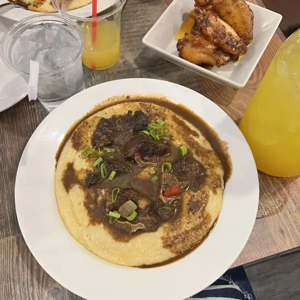 Oxtail over grits with wings and plantains on the table at Carib Soul BK